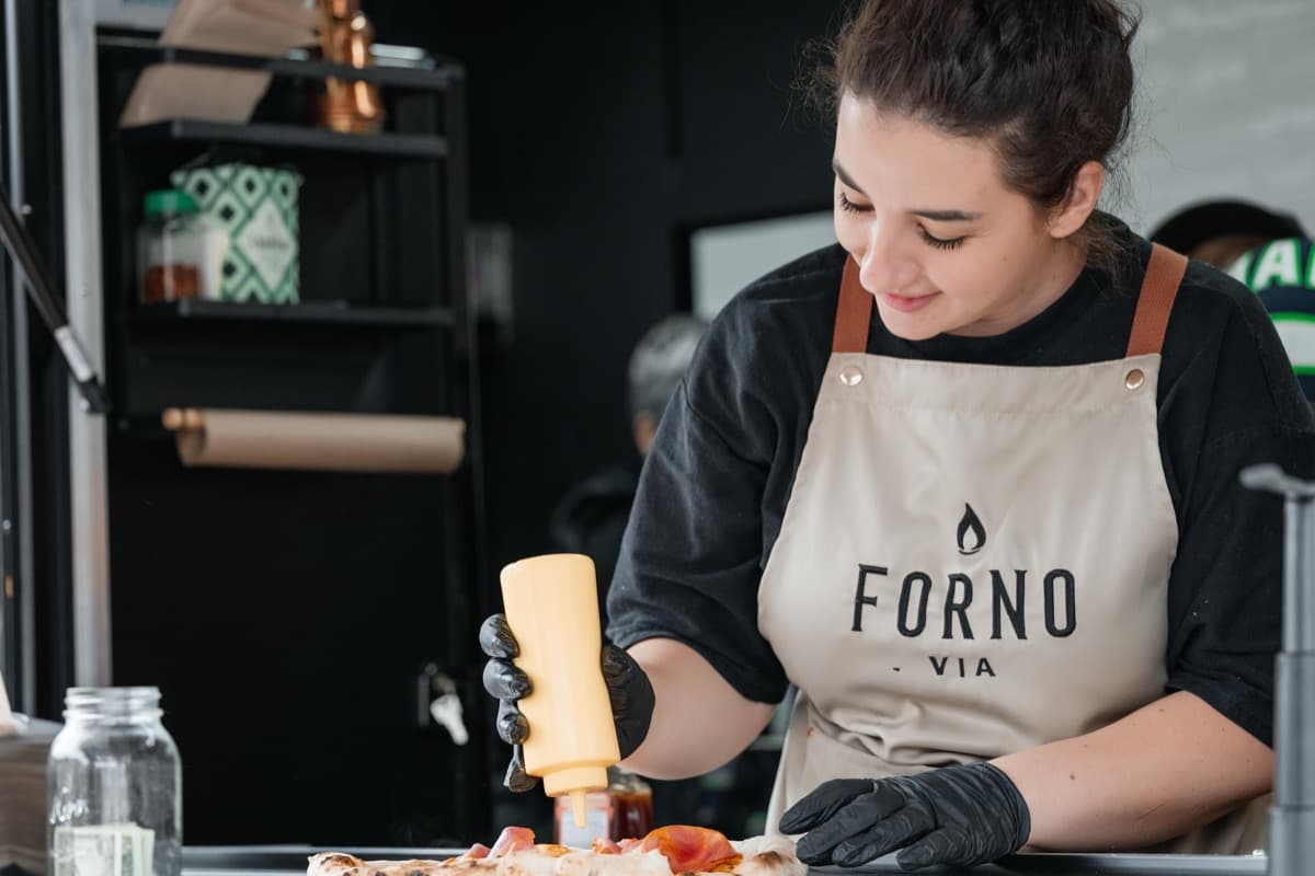 Wood-fired pizza cooking over open flames in Forno Via's mobile oven at a Seattle event
